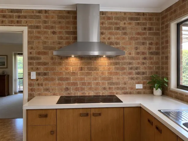 Stainless steel range hood above cooktop on brick kitchen wall in Westleigh